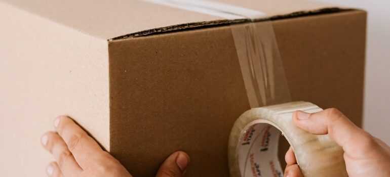 person closing up a moving box with packing tape