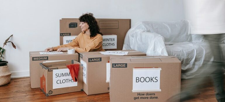 woman sitting on the floor, properly labeled moving boxes around 