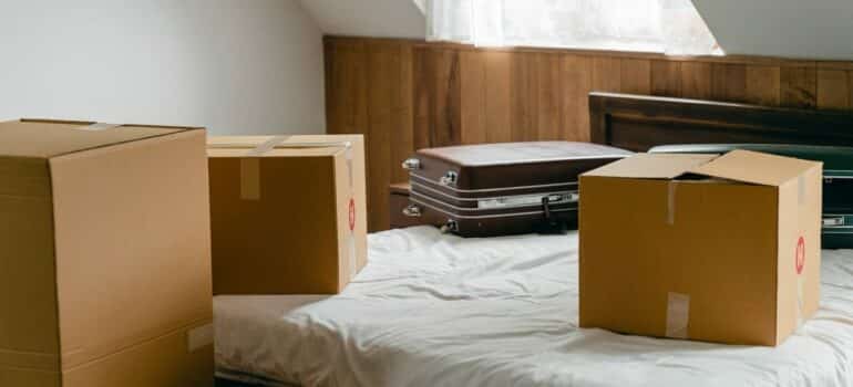 cardboard boxes and suitcases on a bed as expected when you prepare for moving from Texas to NYC