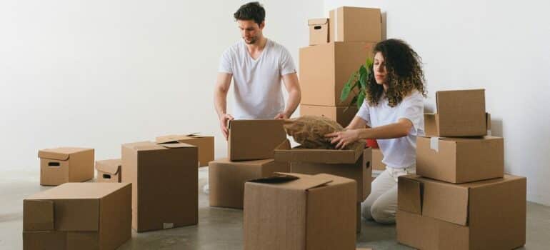 a couple sitting between cardboard boxes while packing their items