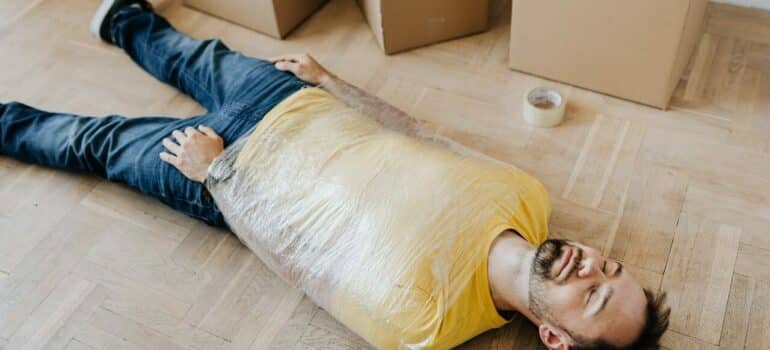 man lies on the floor taped in plastic wrap
