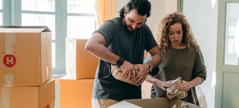 Man and woman wrapping some items and putting them in a box;