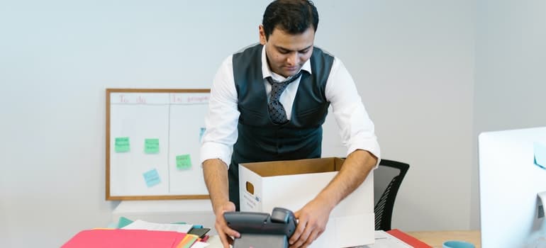 A man in an office packing a phone, while thinking how to pack and move office chair;