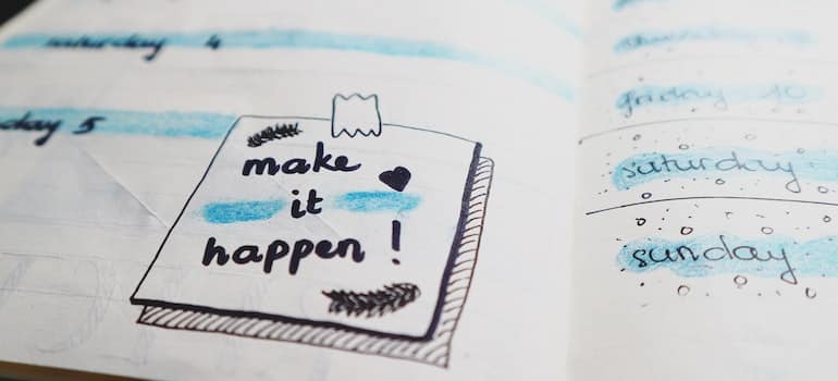 White notebook with a sticker on it which says "make it happen";