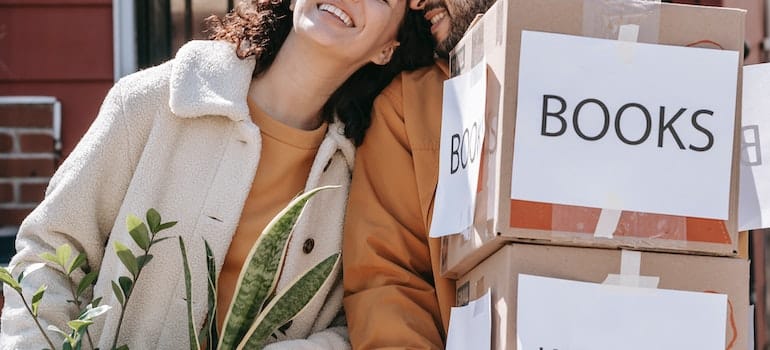A smiling couple carrying moving boxes