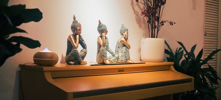three-buddha-sitting-figurines-near-oil-diffuser-on-top-of-piano