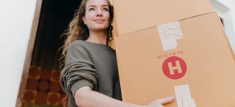 A woman holding boxes, while moving out of the storage, while thinking about choosing the right storage option for your furniture;