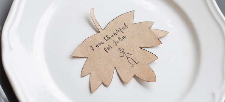 A little paper leaf reading “I am thankful for John” on a plate, one of the cuter thanksgiving crafts to decorate your New Austin home