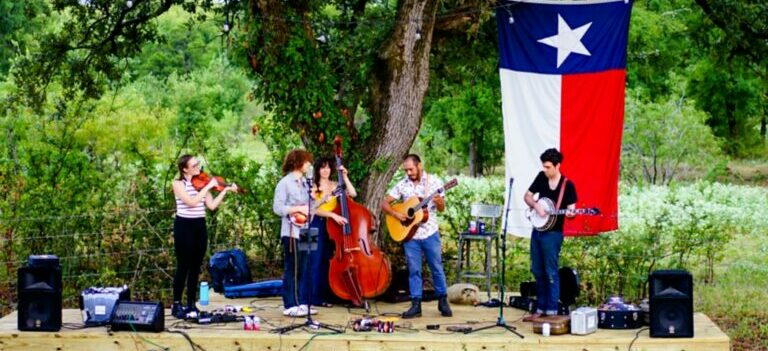 Musicians performing on a stage beside the tree, with Texas flag behind in one of the North Austin neighborhoods 